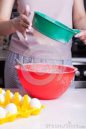 Cooking Easter cake at home in the kitchen. Sifting flour through a green sieve in female hands into a red bowl next to the Stock Photo
