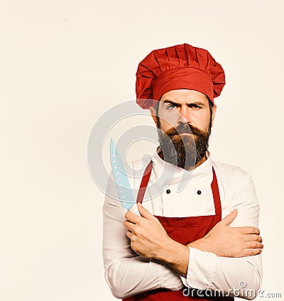 Cooking equipment and cuisine concept. Cook with serious face in burgundy apron and chef hat. Stock Photo
