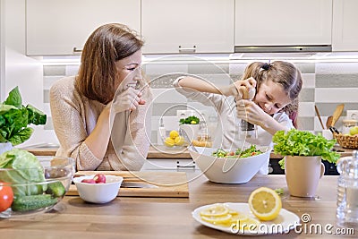 Cooking healthy home meal by family. Girl salts freshly cooked salad, mother looks up and rejoices Stock Photo