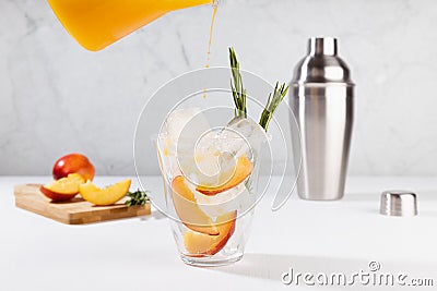 Cooking healthy summer peach juice - cocktail pour of jug in glass with ice, rosemary twig, sugar rim, ingredients in elegant. Stock Photo