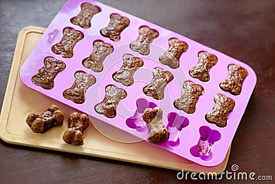 Cooking the homemade biscuits for dogs, bone-shaped in silicone mold, taken out of the oven. Dog treats from liver and carrot. Stock Photo