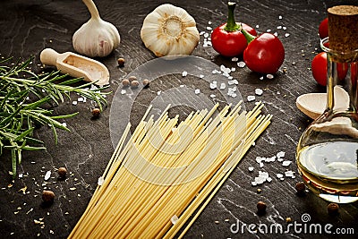 Tomatoes garlic salt olive peppers and pasta on a black table Stock Photo