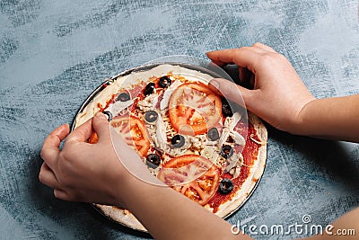 Cooking Italian pizza with tomatoes, chicken, olives on wooden background. Tomato sauce on the dough by woman`s hand Stock Photo