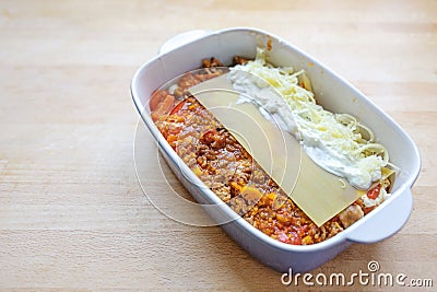 Cooking lasagna, layers of Bolognese sauce, flat pasta sheets, cream or bechamel and cheese in a casserole dish on a wooden Stock Photo