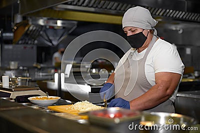 Cooking, profession and people concept - woman in age chef wearing protective black mask on her face while working in Stock Photo