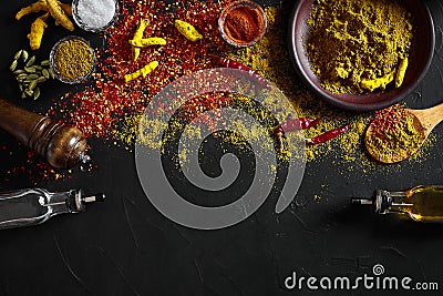 Cooking using fresh ground spices with big and small bowls of spice on a black table with powder spillage on its surface Stock Photo