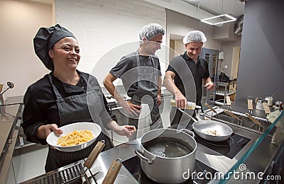 Cooks and chef cooking italian food pasta and smiling at open kitchen inside modern restaurant Editorial Stock Photo