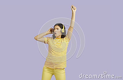 Cool energetic woman in headphones listens to music and dances on pastel purple background. Stock Photo