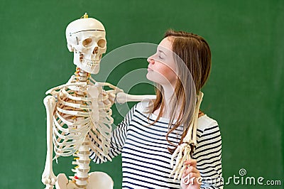 Cool female high school student portrait with an artificial human body skeleton. Student having fun in Biology class. Stock Photo