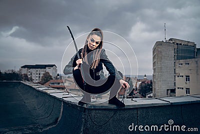 Cool female ninja warrior in leather outfit wielding a Japanese sword on the top of a building Stock Photo