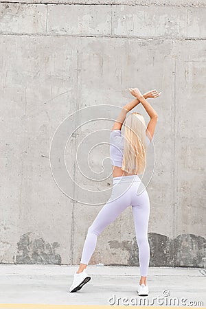 Cool fitness model woman with a beautiful slender figure in fashionable sports clothes and sneakers walks near a gray concrete Stock Photo