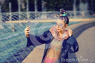 Cool funky hipster young fashion influencer girl with crazy hair and avant garde style taking selfie on street Stock Photo