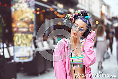 Cool funky young hipster woman with trendy eyeglasses and crazy hair listening music on headphones outdoor Stock Photo