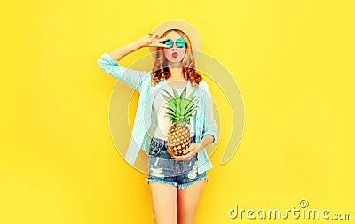 cool girl with pineapple blowing red lips sending sweet air kiss in summer straw hat, sunglasses, shorts on colorful yellow Stock Photo