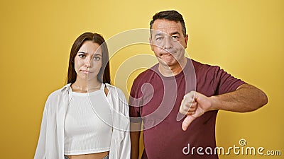 Cool hispanic father and daughter bond over their thumbs down gesture, expressing negative vibes together against an isolated Stock Photo