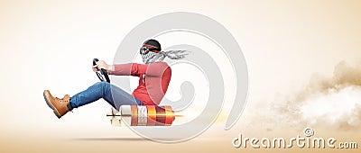 Cool man in stylish goggles and a scarf on his face, drives a car on a rocket engine, on yellow background. Stock Photo