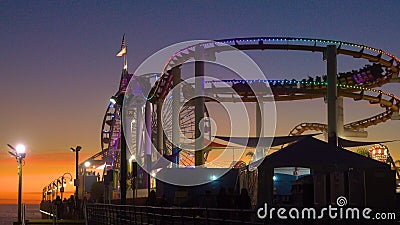 Tourists enjoy a rollercoaster ride in Santa Monica amusement park at sunset Editorial Stock Photo