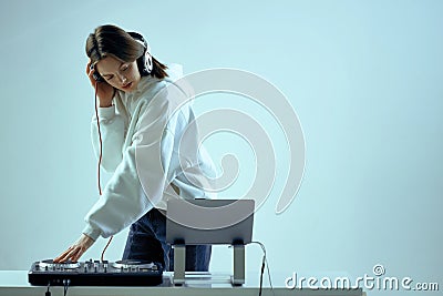 Cool young girl DJ mixes music on a mixing console and laptop, in stylish clothes, on white blue background. Stock Photo