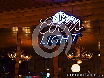 Coors Light beer neon sign with rustic Canadian wooden cabin in the background. Editorial Stock Photo