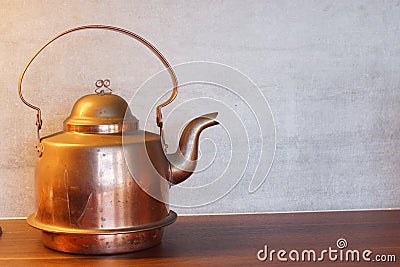 Copper or brass kettle stands on the table opposite the gray wall Stock Photo