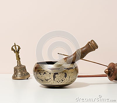 Copper singing bowl and wooden clapper on a white table. Musical instrument for meditation, relaxation, various medical practices Stock Photo