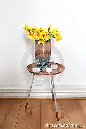 Copper vase on dipped side table with tea lights and yellow daffodils Stock Photo