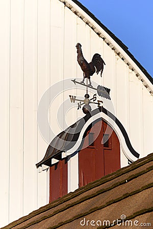 Copper weathervane on red barn cupola, white barn wall as background, blue sky Stock Photo