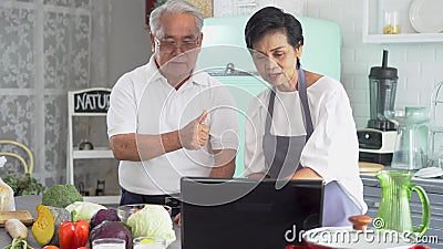 Coppia di anziani asiatici che usa un portatile mentre cucina in cucina a casa 70 anziani uomini e donne in relazione stock footage Coppia di anziani asiatici che usa un portatile mentre cucina in cucina a casa 70 anziani uomini e donne in relazione stock footage