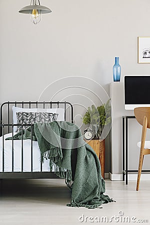 Copy space on empty grey wall of chic bedroom interior with industrial single bed with blue sheets, patterned pillow and dark Stock Photo