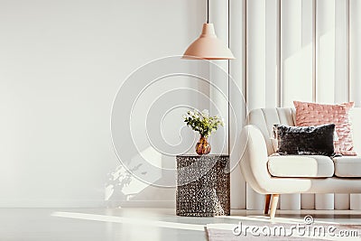 Copy space on white wall of elegant living room with white flowers on glass vase on stylish table next to white sofa Stock Photo