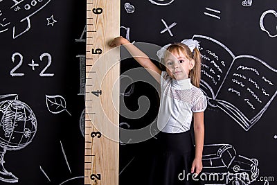 Coquette schoolgirl standing before the chalkboard as a background pointing to the huge scale Stock Photo