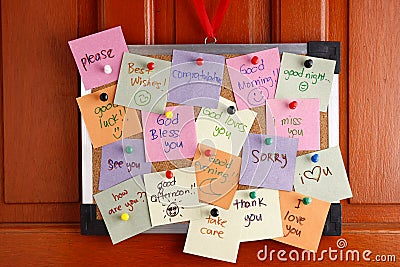 Cork board with messages on colorful papers and push pins hanging by a door Stock Photo