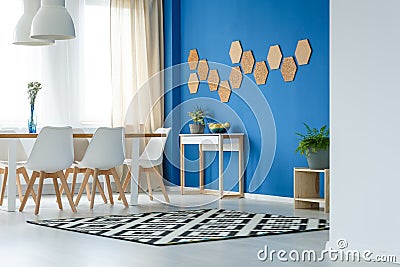 Cork honeycombs on blue wall of trendsetting dining room interior with patterned carpet, plants and white furniture Stock Photo