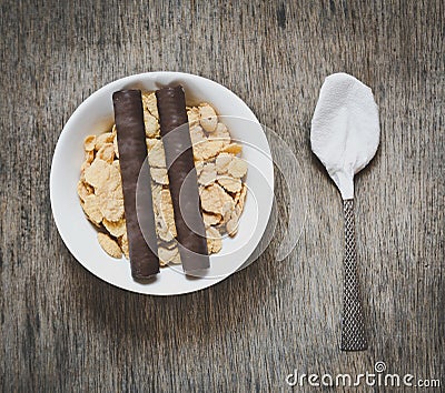 Corn flakes with two chocolate wafer rolls and spoon on a wooden table Stock Photo