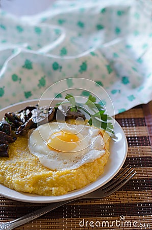 Corn porridge, fried egg, fried mushrooms with onions in a plate on a wicker bamboo napkin Stock Photo