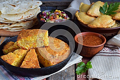 Cornbread and other mexican food - tacos, salsa with tomato, red onion, lime, cilantro, corn and hot pepper sauce, empanadas. Copy Stock Photo