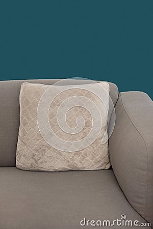 Corner fragment of beige grey upholstered couch with velour decorative cushion on navy blue wall background. Stock Photo