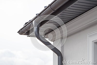 Corner of the house with new gray metal tile roof and rain gutter. Metallic Guttering System, Guttering & Drainage Pipe Exterior Stock Photo