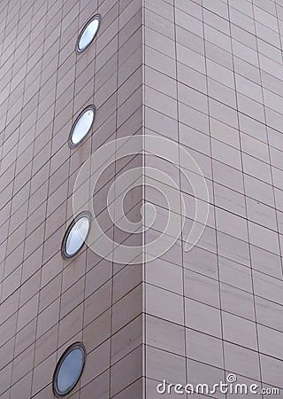 Corner of a large modern commercial building with grey rectangular cladding and round windows Stock Photo