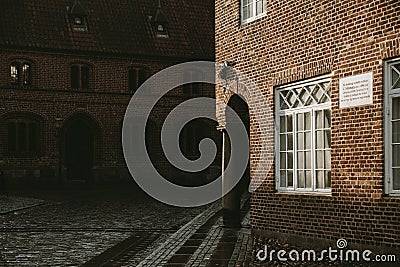 Corner of an old brick house with the underpass supporting by the stone column enlightened with the afternoon sun Stock Photo