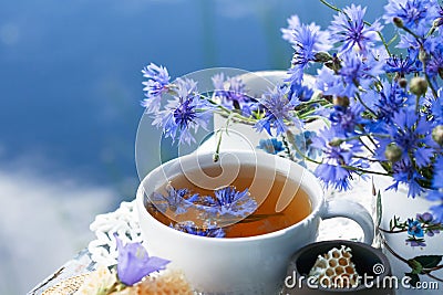 Cornflower herbal tea in white cup on white crochet napkin on table outdoors, healthy cornflower drink Stock Photo