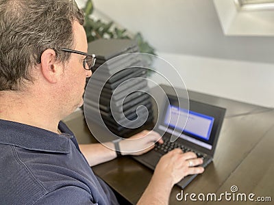A casually dressed caucasian middle aged man is installing a laptop computer with a stack of several more computers next Stock Photo