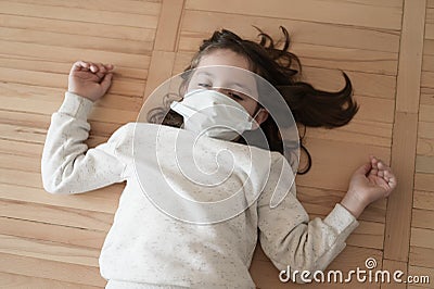 Coronavirus covid-19 epidemic outbreak concept of little suffering girl with medical mask lying on floor at home Stock Photo