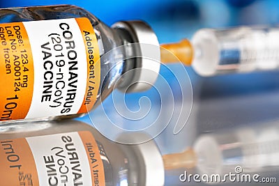 Coronavirus covid-19 vaccine concept - glass bottle with silver cap on glossy white desk, orange syringe injected, blurred blue Stock Photo