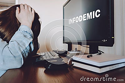 Coronavirus infodemic concept. Frightened woman sitting in front of computer monitor with text infodemic with phone in her hands Stock Photo