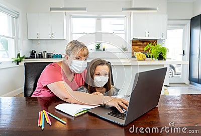 Coronavirus school closures and lockdown. Mum and bored daughter with masks studying online at home Stock Photo