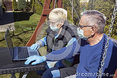 COVID 19 An elderly couple a man and a woman in medical masks in front of a laptop in a garden in a nursing home Stock Photo