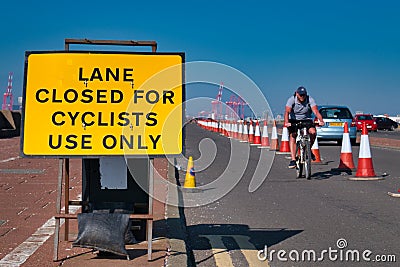 A cyclist approaches a yellow sign advising that a road lane is closed to cars Editorial Stock Photo
