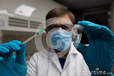 Coronavirus vaccine dose ready for immunisation. Doctor with gloved hands holding a hyperdermic needle and vaccination dose Stock Photo