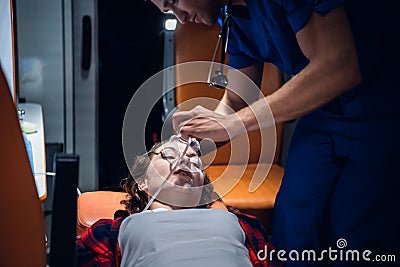 Corpsman puts oxygen mask on woman liyng on stretcher in the ambulance car Stock Photo